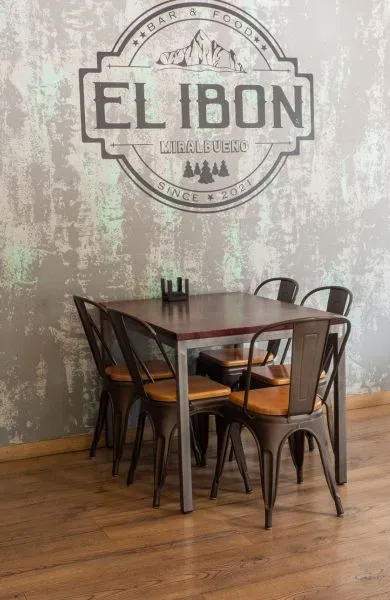 Imagen de una mesa con sillas en el interior en el bar restaurante en Zaragoza el ibón de Miralbueno, con el logo en la pared de fondo